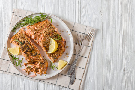 baked salmon fillet with spices, lemon and rosemary on plate on white wooden table with rustic forks, horizontal view from above, flat lay, free spaceの写真素材