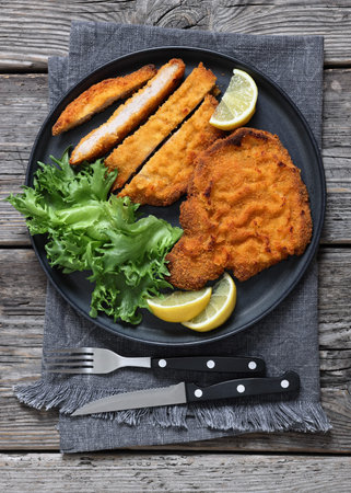 Pork Milanese, breaded thin pork cutlet served with fresh lettuce and lemon wedges on plate on dark...