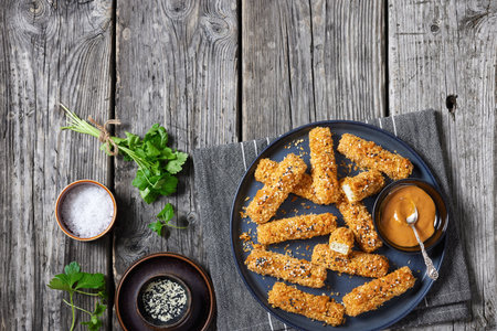 panko breaded tofu fingers sprinkled with sesame seeds served with peanut butter and tahini sauce on plate on rustic wooden table, horizontal view from above, flat lay, free spaceの写真素材