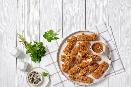 panko breaded tofu sticks sprinkled with sesame seeds served with peanut butter and tahini sauce on plate on white wooden table with and cilantro, horizontal view from above, flat lay, free spaceの写真素材