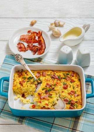 cheesy corn pudding casserole sprinkled with chives and crispy fried bacon in a baking dish with cake shovel on white wooden table, vertical view from aboveの写真素材