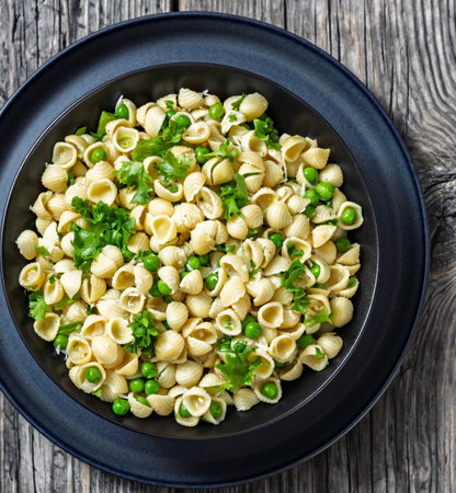 Pasta with green peas, pasta e piselli in black bowl on rustic wooden table, Italian recipe, horizontal view from above, flat lay, close-upの写真素材