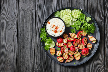 Grilled radishes with cucumber slices and sour cream sauce served on a dark grey plate on a black wooden table, top view, flat lay, free space, real photo, not AI generatedの写真素材