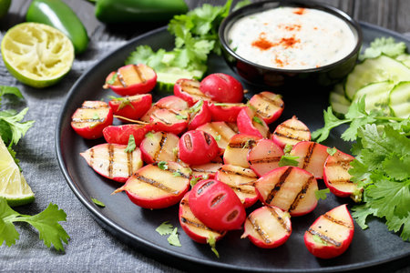 Grilled radishes with cucumber slices and sour cream sauce served on a dark grey plate, horizontal view, close-up, real photo, not AI generatedの写真素材