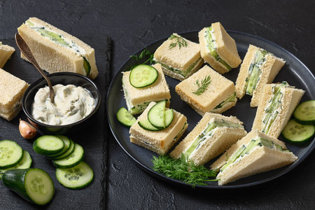 cucumber sandwiches layered with cream cheese spread on black plate with ingredients, horizontal view from above, close-up, real photo, not AI generatedの写真素材