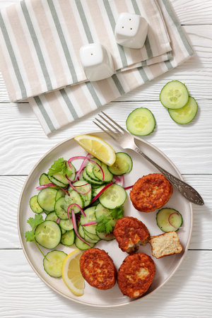 fiskefrikadeller, dutch fishcakes of ground fish fillet served with cucumber salad and lemon on a plate on white wooden table, flat lay, vertical view, real photo, not AI generateの写真素材
