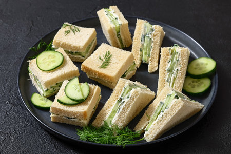 cucumber sandwiches layered with cream cheese spread on black plate on concrete table, horizontal view from above, real photo, not AI generatedの写真素材