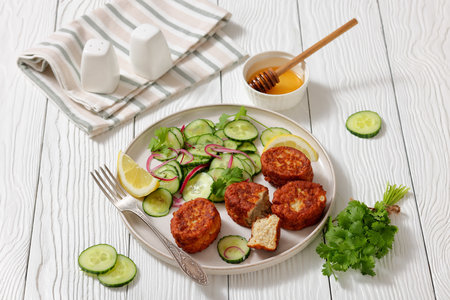 fiskefrikadeller, dutch fishcakes of ground fish fillet served with cucumber salad on a plate with fork on white wooden table, horizontal view from above, real photo, not AI generatedの写真素材