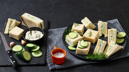 cucumber sandwiches layered with cream cheese spread on black plate with ingredients and knife on a black stone board, horizontal view from above, real photo, not AI generatedの写真素材