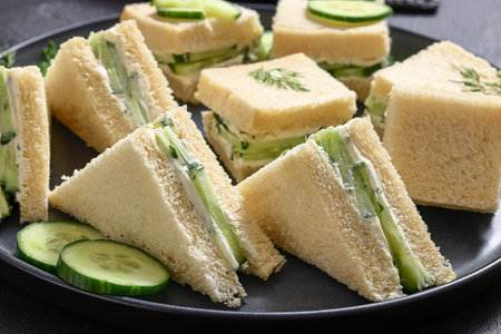 close-up of cucumber sandwiches layered with cream cheese spread on black plate on concrete table, horizontal view from above, real photo, not AI generatedの写真素材