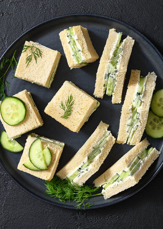 cucumber sandwiches layered with cream cheese spread on black plate on concrete table, horizontal view from above, flat lay, close-upの写真素材