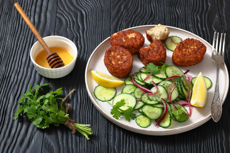 fiskefrikadeller, dutch fishcakes of ground fish fillet served with cucumber salad and lemon on a plate on black wooden table, horizontal view, real photo, not AI generatedの写真素材