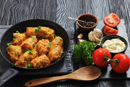 cabbage rolls with quinoa and ground chicken filling on a skillet on dark wood table with spoon, garlic, parsley and mayo, horizontal view from above, real photoの写真素材