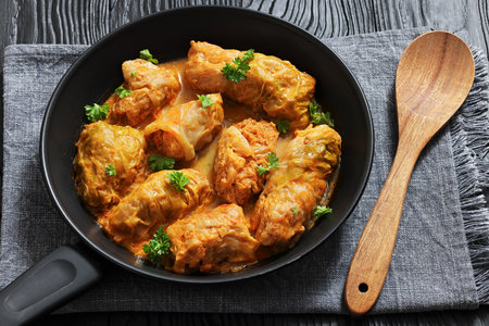 cabbage rolls with quinoa and ground meat filling on a skillet on black wood table with spoon, horizontal view from above, close-up, real photo, not AI generatedの写真素材