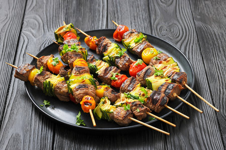 Plate of grilled beef kebabs with zucchini and tomatoes, horizontal view, dark rustic table settingの写真素材