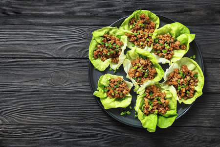 Fresh and Crispy Ground Chicken lettuce wraps of bibb lettuce, minced chicken, spices, and hoisin and soy sauce on a plate on black wooden table, flat lay, free space, not AI generatedの写真素材
