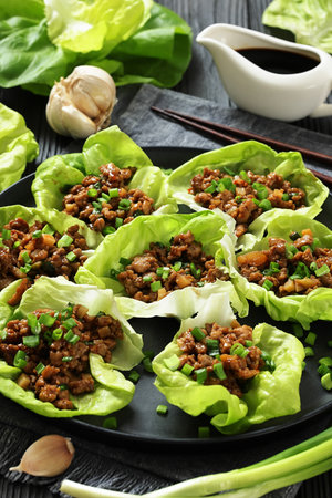 Fresh and Crispy Ground Chicken lettuce wraps of bibb lettuce, minced chicken, spices, and hoisin and soy sauce on a plate on black wooden table, vertical view, close-up, not AI generatedの写真素材
