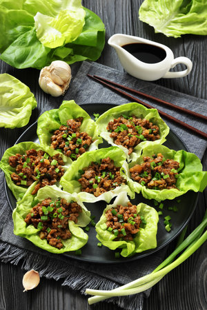 Fresh and Crispy Ground Chicken lettuce wraps of bibb lettuce, minced chicken, spices, and hoisin and soy sauce on a plate on black wooden table, vertical view, not AI generatedの写真素材