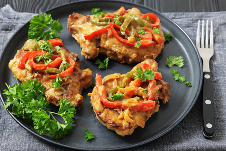 pork chops topped with bell pepper cream gravy on a plate on black wood table with parsley, fork and knife, horizontal view, close-up, real photo, not AI generatedの写真素材