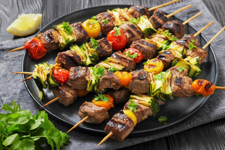grilled beef and vegetable skewers on a rustic plate, set on a dark wooden table, close-up, horizontal view, real photographyの写真素材