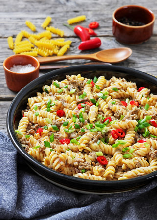 creamy ground beef pasta, cheeseburger fusilli pasta sprinkled with green onion and chili pepper in a bowl on rustic grey wood table, vertical view, close-up, not AI generatedの写真素材