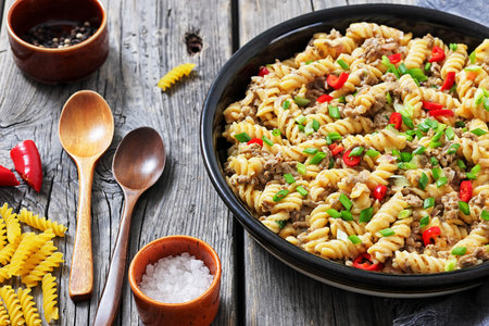 creamy ground beef pasta, cheeseburger fusilli pasta sprinkled with green onion and chili pepper in a bowl on rustic grey wood table with spoons, horizontal view, not AI generatedの写真素材