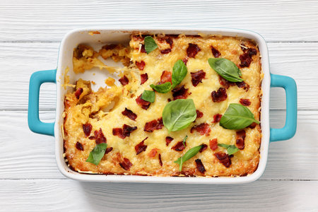 twice baked potato casserole with fried bacon and cheddar cheese in a baking dish on white wood table, horizontal view, flat lay, close-up, not AI generatedの写真素材