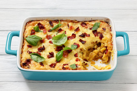 twice baked potato casserole with fried bacon and cheddar cheese in a blue ceramic baking dish on white wood table, horizontal view, close-up, not AI generatedの写真素材