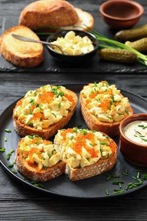 deviled egg salad and red caviar on toast served on a plate with mayo mustard sauce on black wood table with ingredients, vertical view, close-up, not AI generatedの写真素材