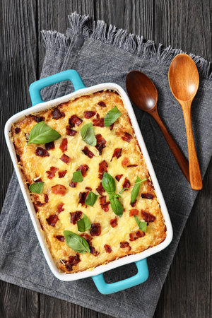 twice baked potato casserole with fried bacon and cheddar cheese in a baking dish on black wood table with spoons and napkin, vertical view, flat lay, free space, not AI generatedの写真素材