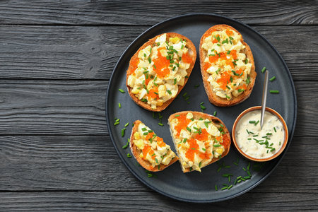 deviled egg salad and red caviar on toast served on a plate with mayo mustard sauce on black wood table, horizontal view, flat lay, free space, not AI generatedの写真素材