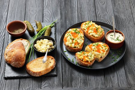 deviled egg salad and red caviar on toast served on a plate with mayo mustard sauce on black wood table with ingredients, horizontal view, not AI generatedの写真素材