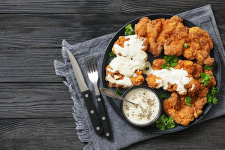 Deep fried Southern chicken thighs on dark grey plate with thick milk pepper gravy on black wooden table with cutlery, top view, flat lay, free space, real photo, not AI generatedの写真素材