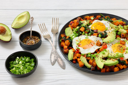 fried Sweet potato cubes served with sunny-side-up eggs and fresh avocado slices on a plate on white wooden table, close-up, not AI-generatedの写真素材