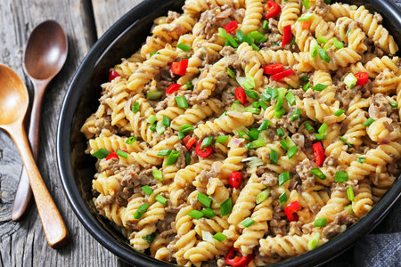 creamy ground beef pasta, cheeseburger fusilli pasta sprinkled with green onion and chili pepper in a bowl on rustic grey wood table with spoons, dutch angle view, close-up, not AI generatedの写真素材