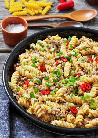 close-up of creamy ground beef pasta, cheeseburger fusilli pasta sprinkled with green onion and chili pepper in a bowl on rustic grey wood table, vertical view, not AI generatedの写真素材