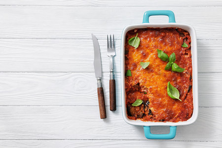 Eggplant Parmigiana, slices of eggplant layered with marinara sauce, parmesan and mozzarella cheese in baking dish on white wood table, flat lay, free space, not AI generatedの写真素材