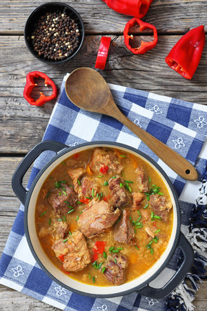 delicious meat stew of beef and pork in dutch oven pot on rustic wood table with kitchen towel and spoon, vertical view from above, close-up, not AI generatedの写真素材
