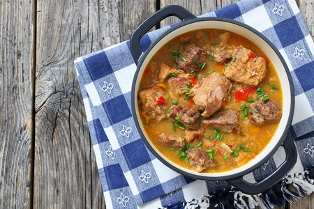 braised meat stew of beef and pork in dutch oven pot on rustic wood table with kitchen towel,horizontal view from above, flat lay, free space, not AI generatedの写真素材