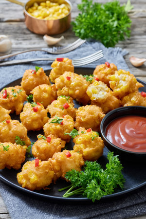 corn nuggets sprinkled with red pepper and parsley on a plate with tomato sauce on rustic grey wood table with forks and ingredients, american cuisine, vertical view, close-up, not AI generatedの写真素材