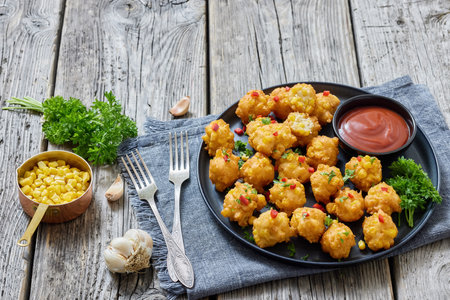 corn nuggets sprinkled with red pepper and parsley on a plate with tomato sauce on rustic grey wood table with forks and ingredients, american cuisine, horizontal view, not AI generatedの写真素材