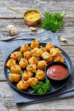 corn nuggets sprinkled with red pepper and parsley on a plate with tomato sauce on rustic grey wood table with forks and ingredients, american cuisine, vertical view, not AI generatedの写真素材