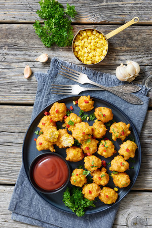 deep fried corn nuggets sprinkled with red pepper and parsley on a plate with tomato sauce on rustic grey wood table with forks and ingredients, american cuisine, vertical view, not AI generatedの写真素材