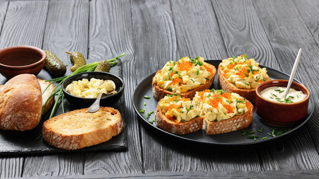 deviled egg salad and red caviar on toast served on a plate with mayo mustard sauce on black wood table with ingredients, horizontal view, not AI generatedの写真素材