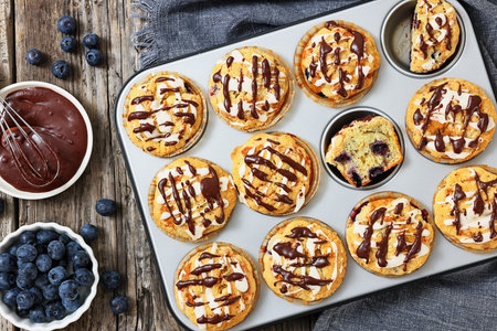 lemon blueberry muffins in a muffin pan sprinkled with lemon chocolate glaze on rustic wood table with fresh berries, horizontal view, flat lay, not AI generatedの写真素材