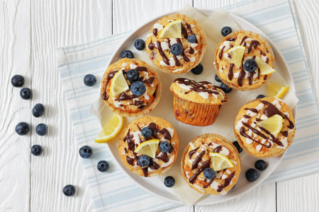 blueberry muffins sprinkled with lemon chocolate glaze on a white plte on white wood table with fresh berries, top view, flat lay, not AI generatedの写真素材