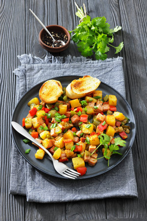 denver-style fried cubed potatoes with ham, bell peppers and onion sprinkled with green onion on a plate with toasts and fork, vertical view from above, american cuisineの写真素材