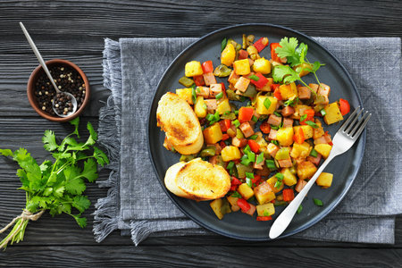 denver-style fried cubed potatoes with ham, bell peppers and onion sprinkled with green onion on a plate with toasts and fork, flat lay, not AI generatedの写真素材