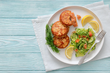 Smoked salmon burgers, patties, or cakes served with coleslaw and lemon wedges with fork on a white...