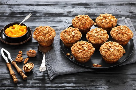 mashed sweet potato muffins with streusel nut topping and cream cheese filling on a plate on dark wood table with ingredients, landscape view from aboveの写真素材